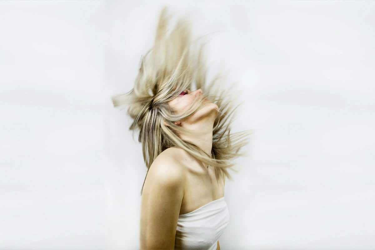 Jonge blonde vrouw gooit haar lange haren naar achteren en door de sluitertijd is de beweging van haar haren mooi vastgelegt