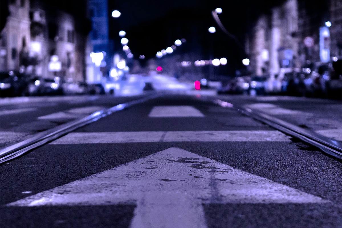 Een straat gefotografeerd in het donker met op de voorgrond een pijl en in de achtergrond de stad met verlichting